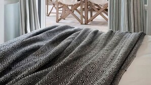 Habitación con cama, vista a un área exterior de comedor con mesa y sillas, y estructura de techo de madera.