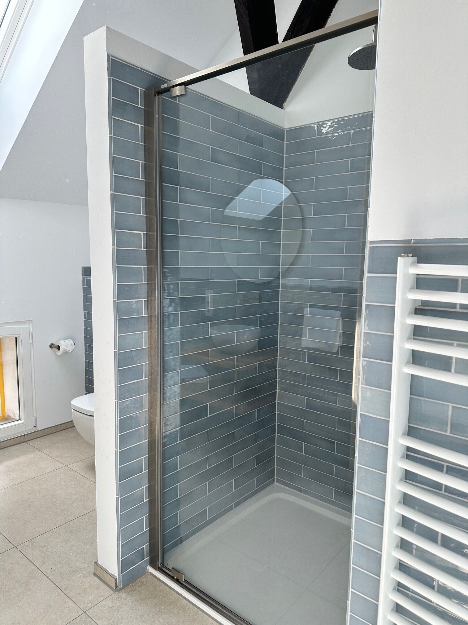 A modern bathroom with a glass shower enclosure, grey tiled walls, and a white toilet.