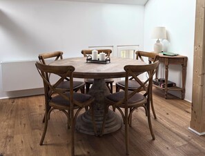 Ein runder Holztisch mit sechs Stühlen, einer Lampe und einem kleinen Bücherregal.