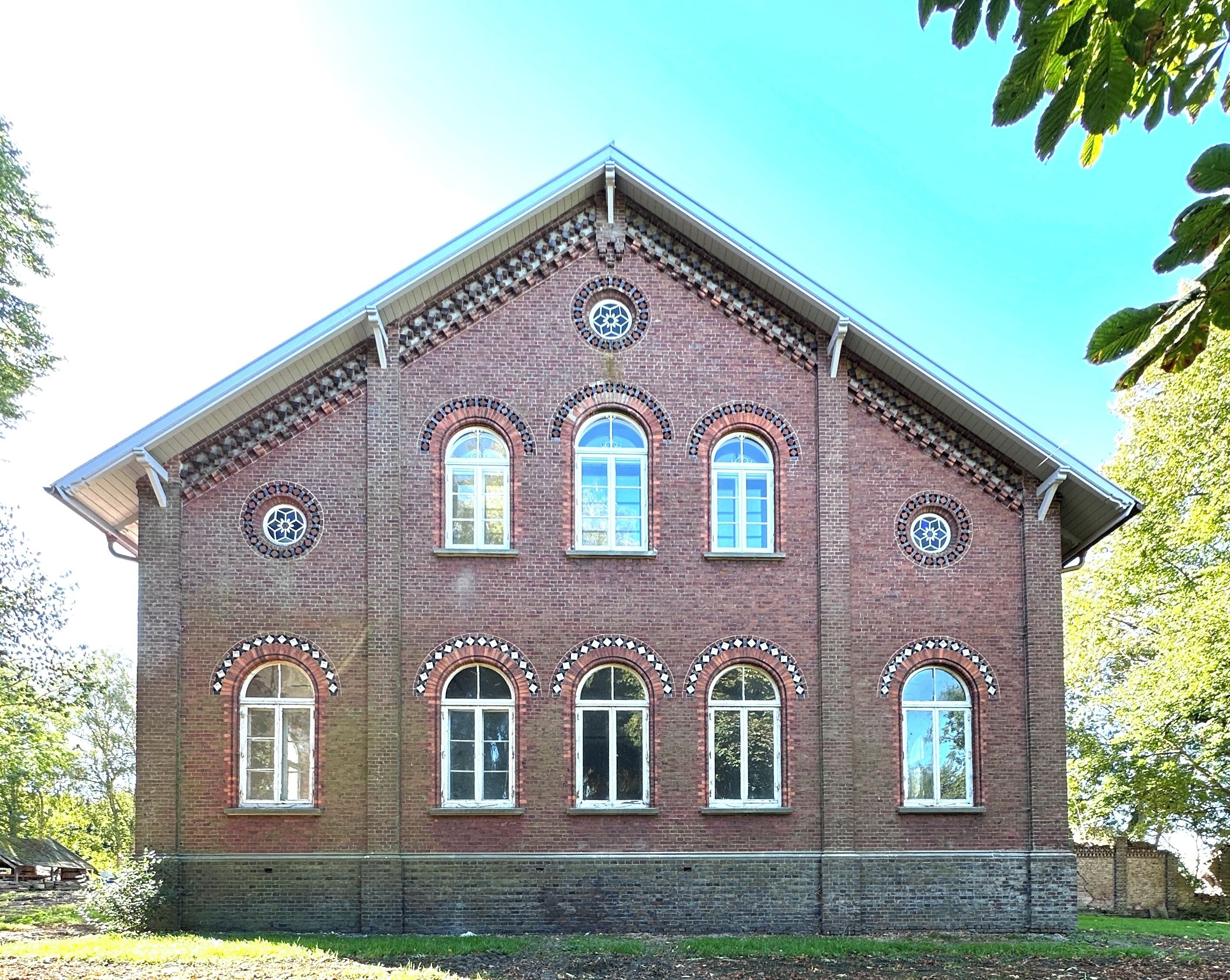 A brick building with a gabled roof, multiple arched windows, and decorative circular patterns around the windows.