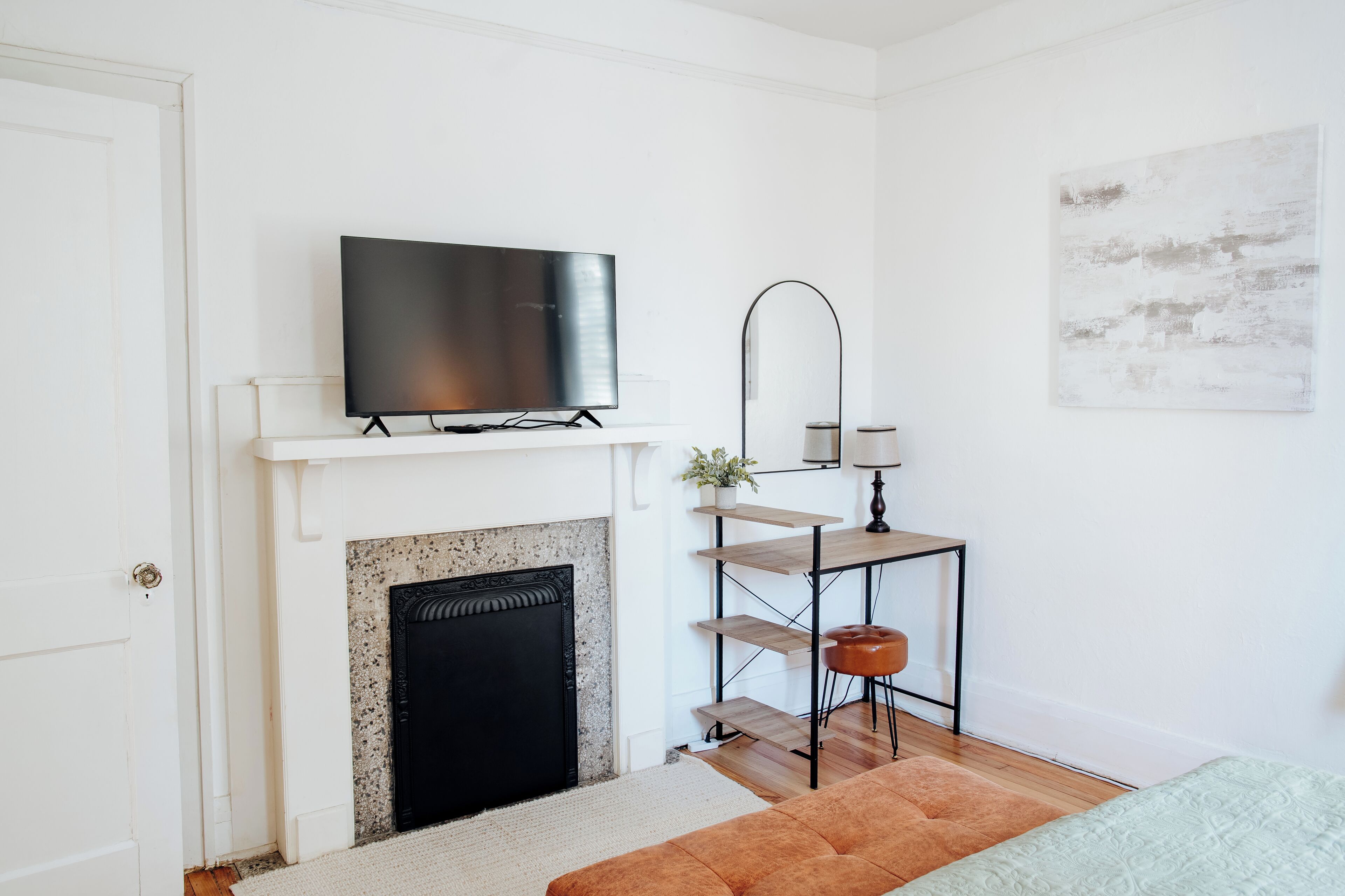 A modern living room with a fireplace, a mounted TV, a small table with a lamp, and a painting on the wall.