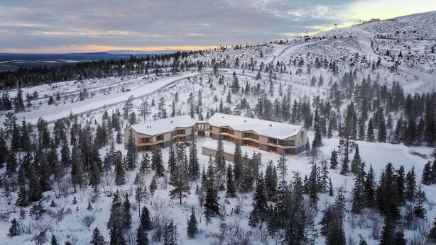 Um edifício moderno de vários andares, rodeado por uma floresta coberta de neve.