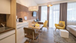 Una habitación de hotel moderna con zona de comedor, sofá y televisor en la pared.