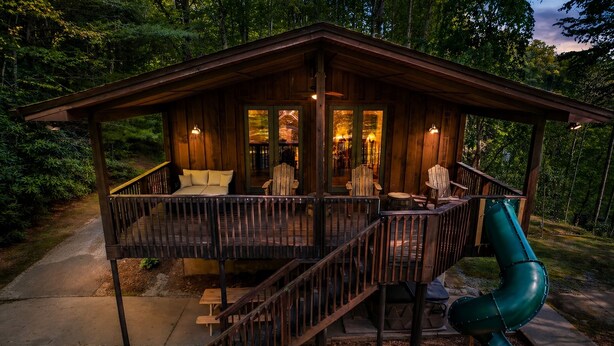 Une cabane en bois avec une véranda, un escalier et un toboggan.