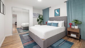 A modern bedroom with a large bed, a nightstand with a lamp, a potted plant, and a California map on the wall.