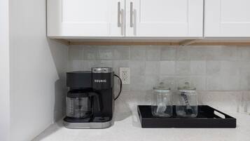 Pieni keittiönurkkaus, jossa on Keurig-kahvinkeitin, kaksi lasipurkkia ja valkoiset kaapit.