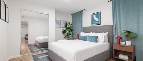 A modern hotel room with a large bed, a bedside table, a mirror, and a view of the hallway.
