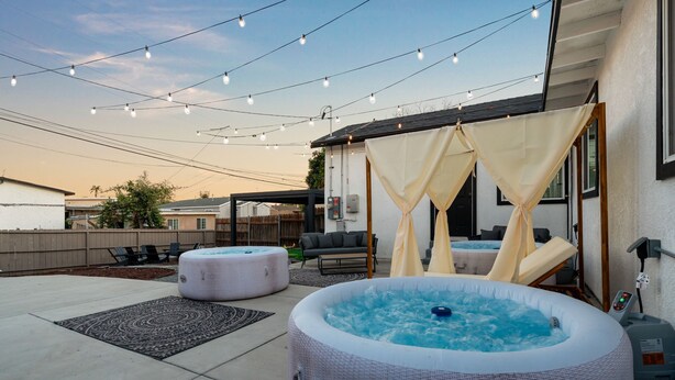 An outdoor patio with two hot tubs, string lights, and a canopy.