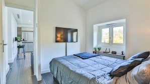 Een slaapkamer met een bed, een aan de muur bevestigde televisie, een raam met uitzicht en een klein bureau met een plant.