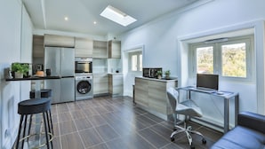 Een moderne keuken met een ingebouwde wasmachine, een eethoek met een glazen tafel en een groot raam met uitzicht op bomen.