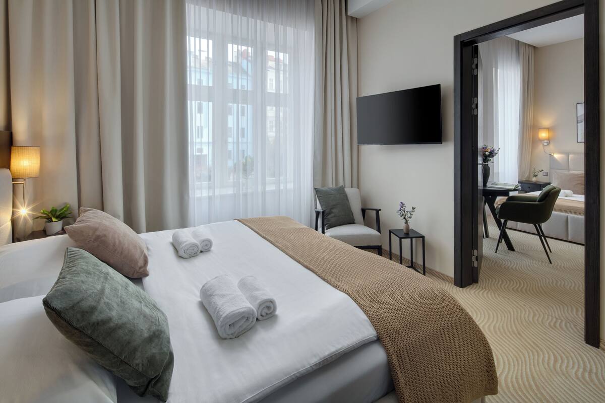 A hotel room with a bed, a desk, a chair, a TV, and a view of the city through the window.