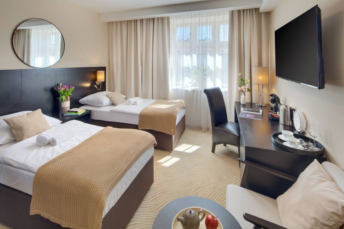 A hotel room with two beds, a desk, a chair, a TV, and a window with curtains.