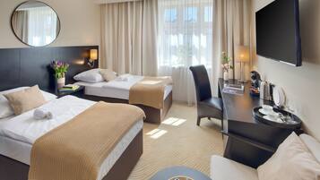 A hotel room with two beds, a desk, a chair, a TV, and a window with curtains.