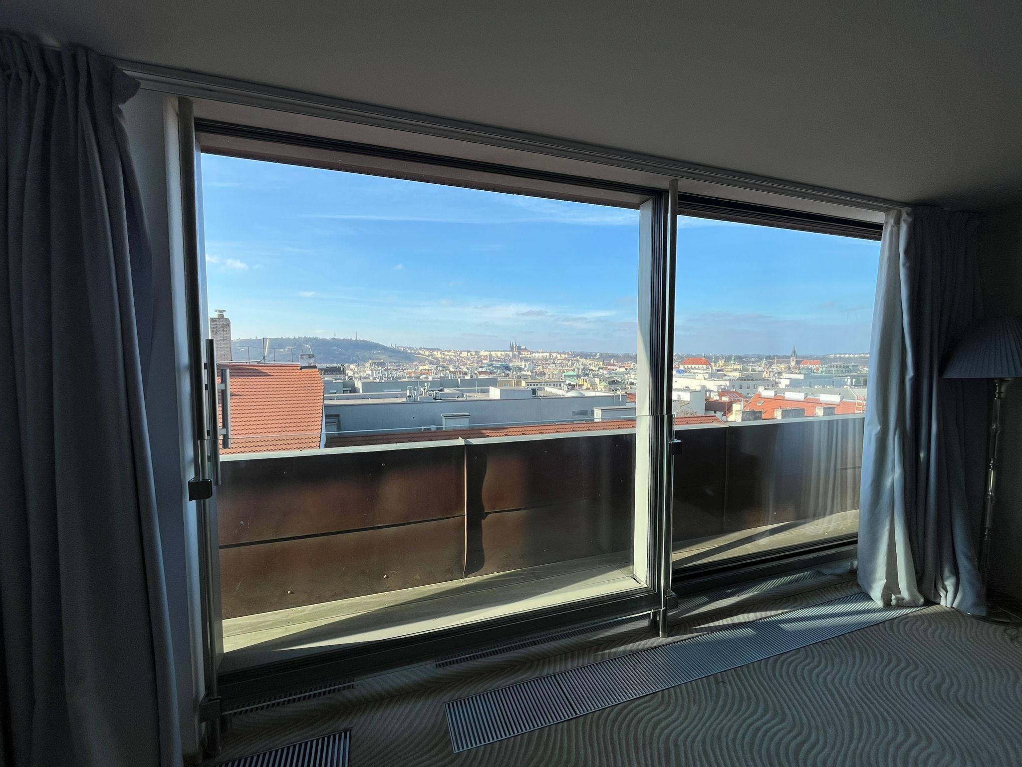 A room with a large sliding glass door leading to a balcony with a city view.