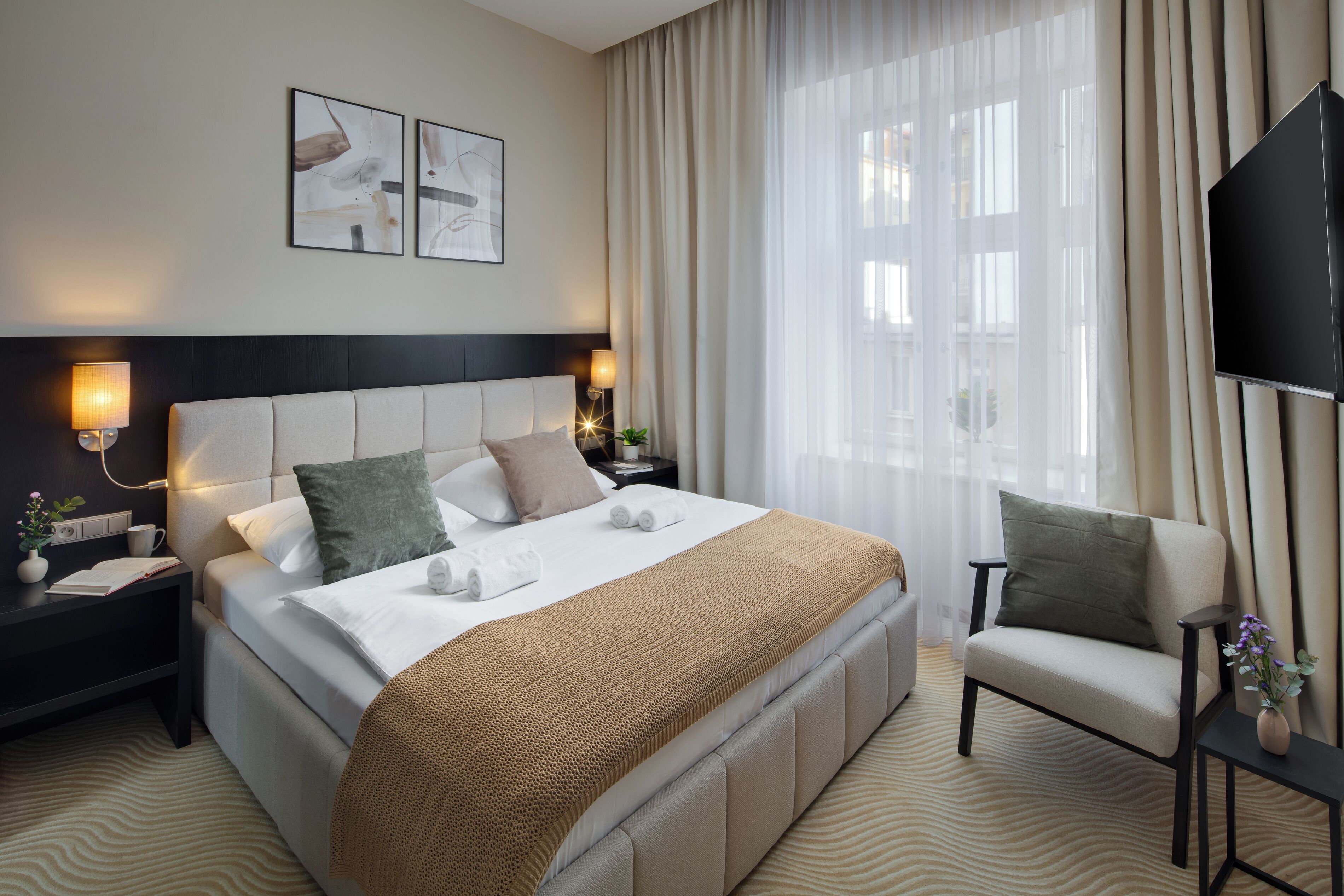 Une chambre d’hôtel avec un grand lit, un canapé, une télévision et des œuvres d’art accrochées au mur.