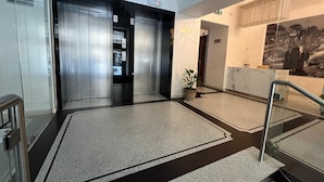 Ein modernes Interieur mit Aufzug, einer Topfpflanze und einer Marmorwand mit Wandgemälde.