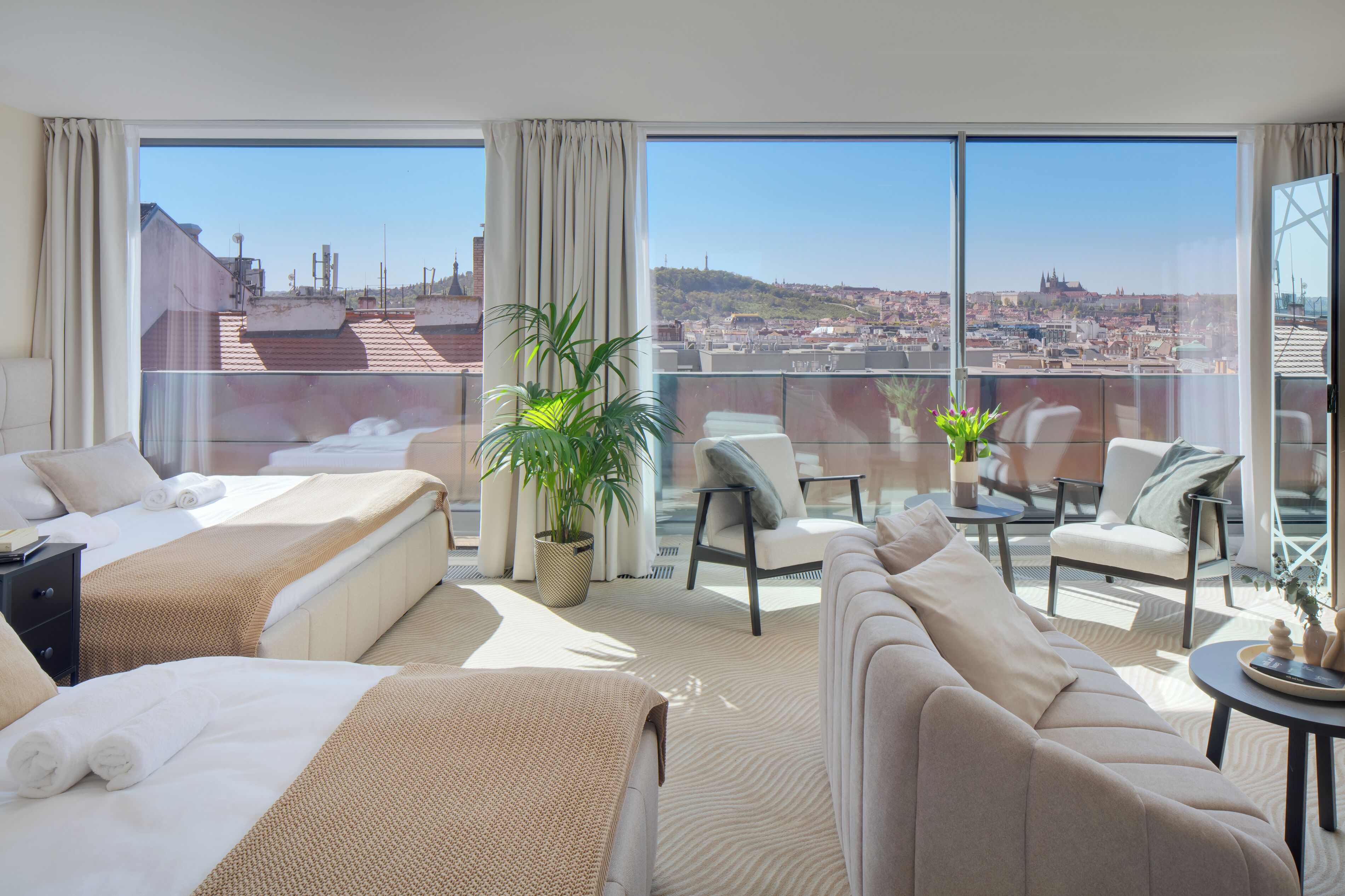 A hotel room with a large balcony, a bed, a sofa, and a dining table.