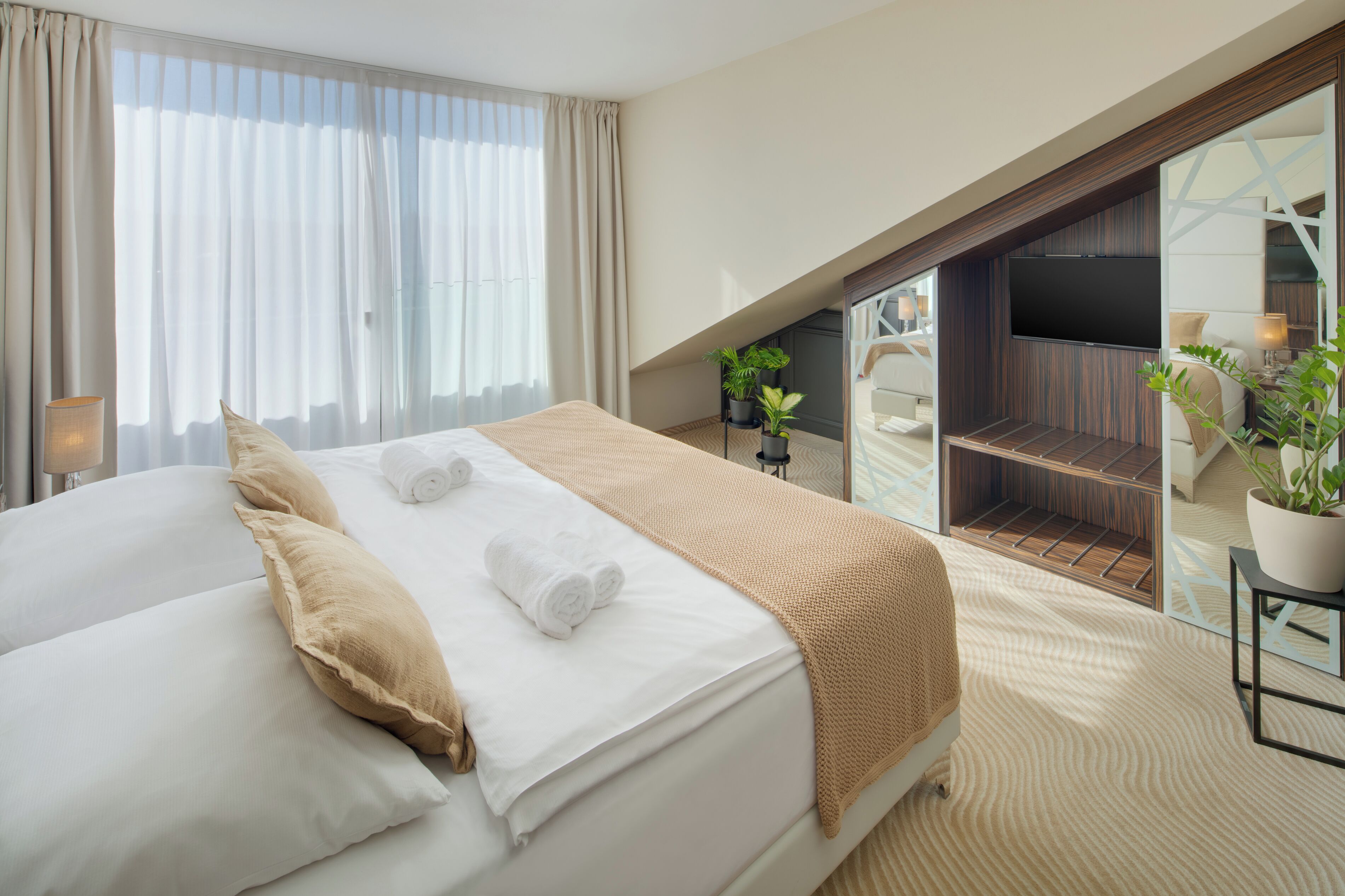 Una camera d'albergo con un letto grande, una TV, un balcone con posti a sedere e una pianta su un tavolino.