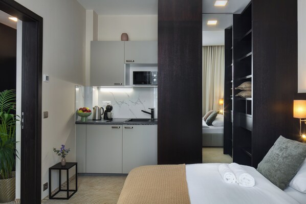A hotel room with a bed, a small kitchenette, a bathroom, and a view of a cityscape. - Wenceslas Hotel & Apartments (Prague)