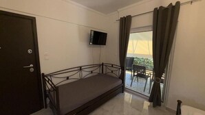 Ein kleines Zimmer mit einem Einzelbett, einem an der Wand befestigten Fernseher und einer Schiebeglastür, die zu einem Außenbereich führt.