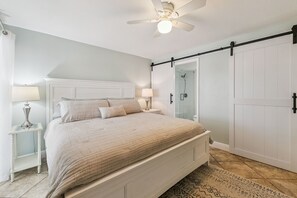A bedroom with a bed, nightstands, a ceiling fan, a sliding door, and a patterned rug. - Southeast Serenity-Luxury Oceanfront Condo | New Smyrna Beach 1 Bedroom | 1 Bathroom (New Smyrna Beach)