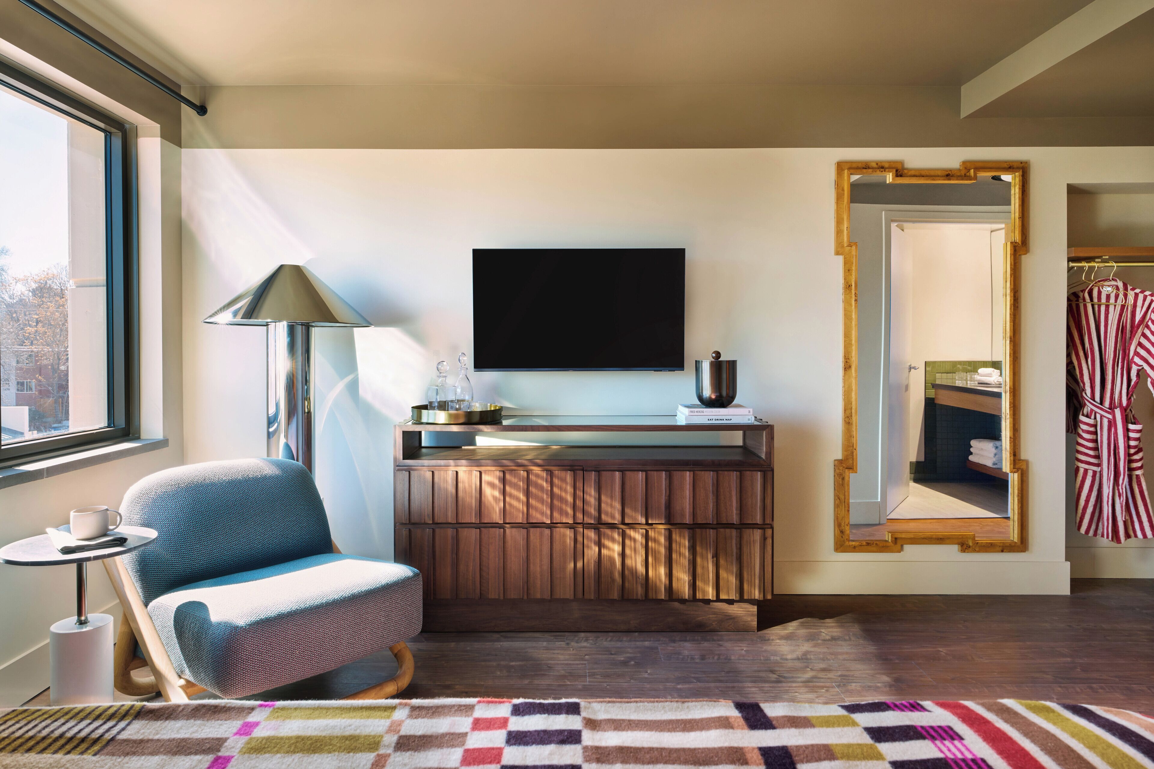A modern room with a wooden console table, a television, a mirror, a chair, and a window.