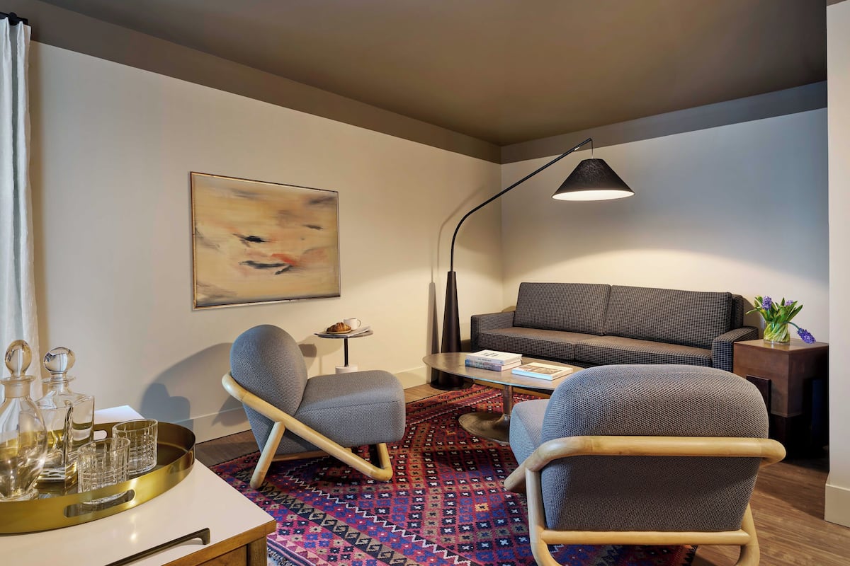 Una sala de estar moderna con un sofá, dos sillones, una mesita de centro, una lámpara de pie y un tapete estampado.