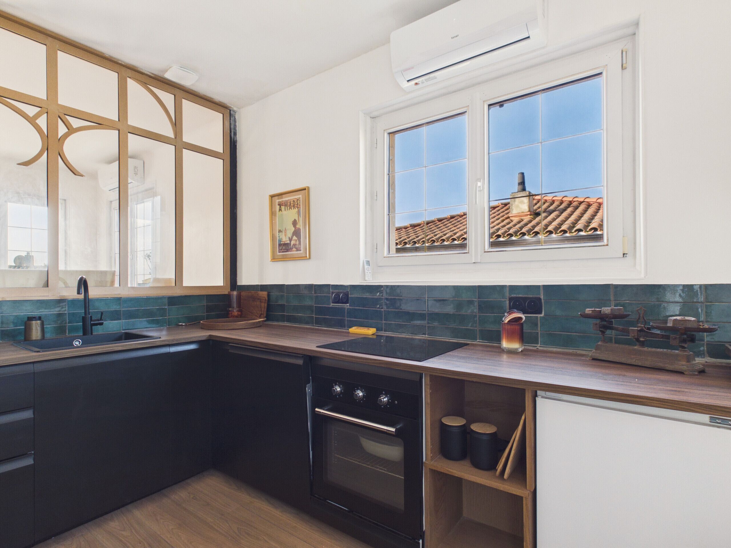 Een moderne keuken met een zwart fornuis, een gootsteen en een raam met uitzicht op een pannendak.