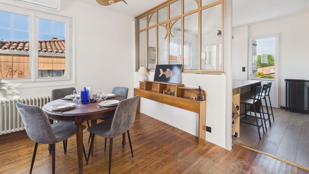 A dining area with a wooden table and chairs, a wall-mounted shelf with decorative items, and a large window with a view of the roof tiles outside. - Comfortable house for 8 with garden (Saint-Gilles-Croix-de-Vie)