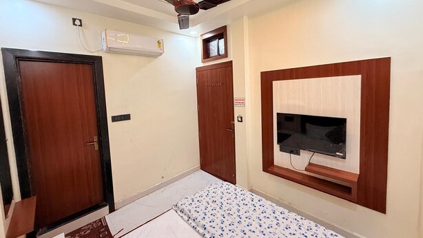 Een slaapkamer met een bed, een plafondventilator, een airconditioning en een aan de muur bevestigde televisie, plus een deur.