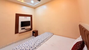 Een slaapkamer met een bed, een plafondventilator, een televisie aan de muur en een klein nachtkastje.