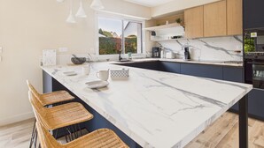 A modern kitchen with a large marble island, bar stools, wooden cabinets, and a window overlooking a garden. - 100m from the beach – House for 8 with garden (Fouesnant)