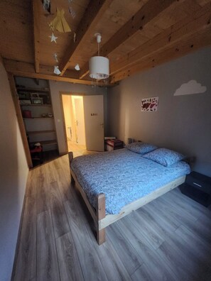 Un dormitorio con techo de madera, una cama con ropa de cama estampada, una mesita de noche y una pared decorada con nubes.