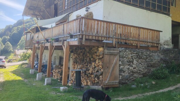 Un chalet rustique doté d’un balcon en bois, de fondations en pierre et d’un chien au premier plan.