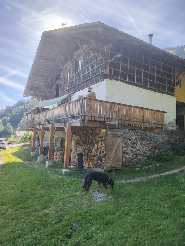 A rustic chalet with a wooden balcony, stone foundation, and a dog in the foreground.