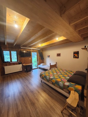 A wooden cabin bedroom with a bed, a desk, a radiator, and a window.