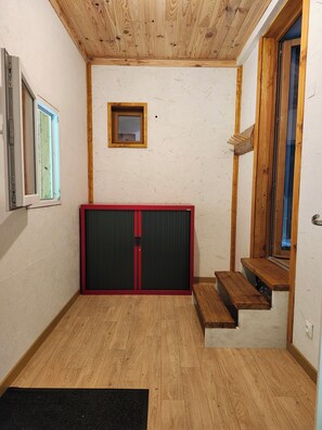 Una habitación con techo de madera, puerta corredera, ventanal pequeño y escalera de madera.