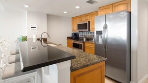 A modern kitchen with a central island, stainless steel appliances, and wooden cabinets. - Beachfront 3BR, 2BA Apollo condo with pool, WiFi, and heated Gulf views. (Marco Island)