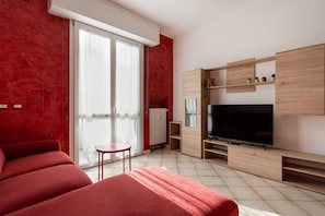 A modern room with a large flat-screen TV, a sliding glass door to a balcony, and a red sofa. - GuestHost - Cozy and bright 55 square meters apartment, perfect for four people, located on the third floor of a building with an elevator (NOT accessible to disabled guests).The property enjoys a strategic location, near Viale Certosa and Corso Sempione (Milan)