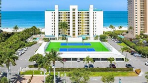 A multi-story hotel with a tennis court, parking area, and a view of the beach. - Beachfront 3BR, 2BA Apollo condo with heated pool and WiFi. (Marco Island)