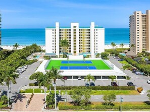 Ein mehrstöckiges Hotel mit Tennisplatz, Parkbereich und Blick auf den Strand.