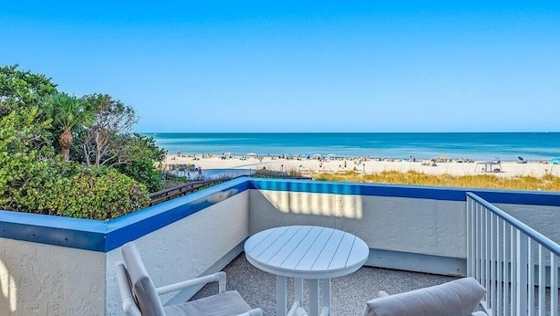A balcony with a view of a beach, a round table, and two chairs. - Beachfront 3BR, 2BA Apollo condo with heated pool and WiFi. (Marco Island)