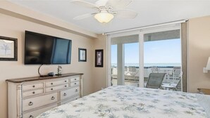 A bedroom with a bed, a dresser, a TV, and a balcony with a view of the ocean. - Beachfront 3BR, 2BA Apollo condo with heated pool and WiFi. (Marco Island)