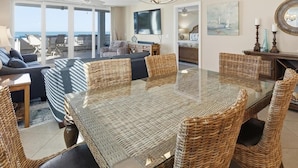 A spacious living room with a large glass-top dining table surrounded by wicker chairs, a sofa, and a TV. - Beachfront 3BR, 2BA Apollo condo with heated pool and WiFi. (Marco Island)