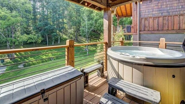 A wooden deck with a hot tub, wooden railings, and a view of a forested area. - Ripple Run at Eagles Nest - pets allowed, hot tub, grill, community amenities, Fish Camp section (Banner Elk)