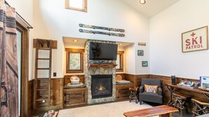 A cozy living room with a stone fireplace, wooden furniture, and a ski patrol sign on the wall. - Ripple Run at Eagles Nest - pets allowed, hot tub, grill, community amenities, Fish Camp section (Banner Elk)