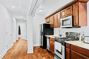 A modern kitchen with wooden cabinets, stainless steel appliances, and a wooden floor. - Prime 3BR Philly Pad Fits 6 Guests Walk Everywhere (Philadelphia)