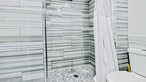 Een moderne badkamer met een douchecabine van glas, een betegelde vloer en een wit toilet.