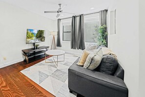 A modern living room with a flat-screen TV, a sofa, a coffee table, and a floor lamp. - Prime 3BR Philly Pad Fits 6 Guests Walk Everywhere (Philadelphia)