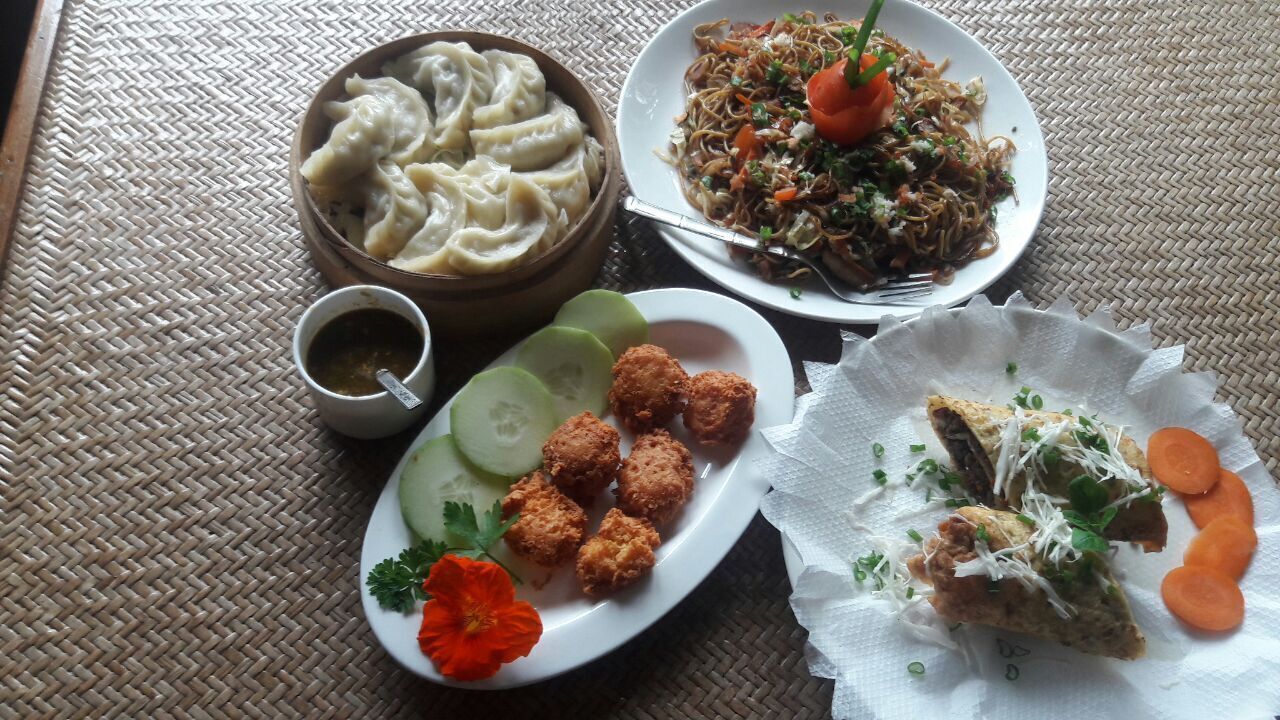 A table with various dishes including dumplings, noodles, fried items, and a small cup of tea.